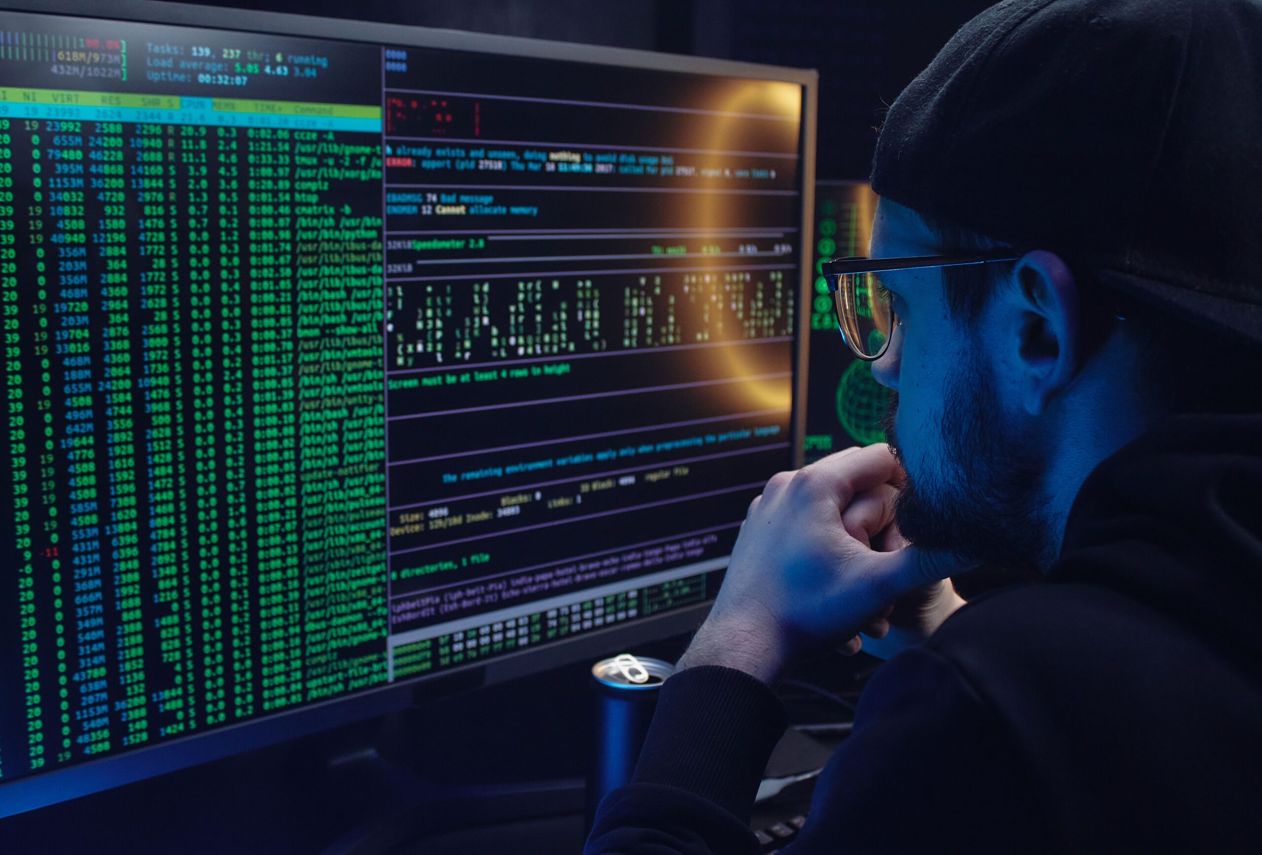 Férfi két monitoron programkódot és adatokat néz egy félhomályos szobában